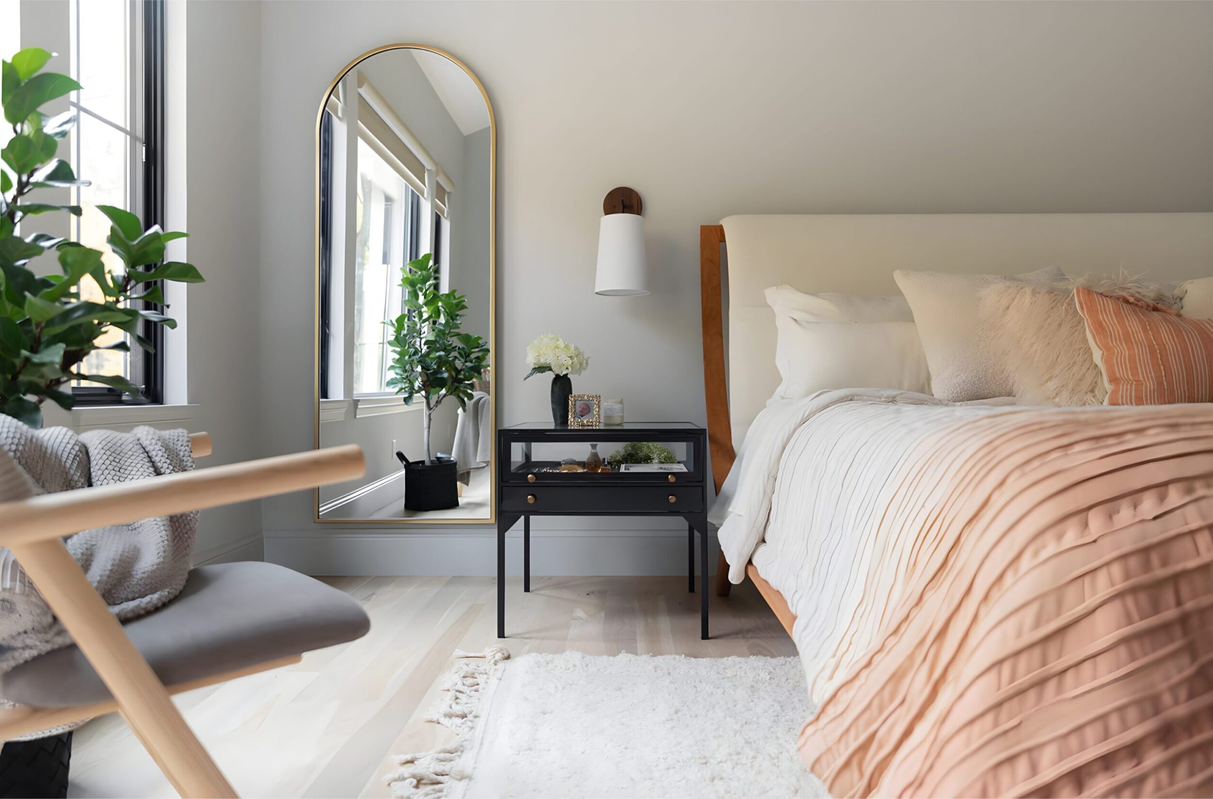 Elegant master bedroom with tall arched mirror, indoor plant, black nightstand, and bed styled with pleated blush pink bedding