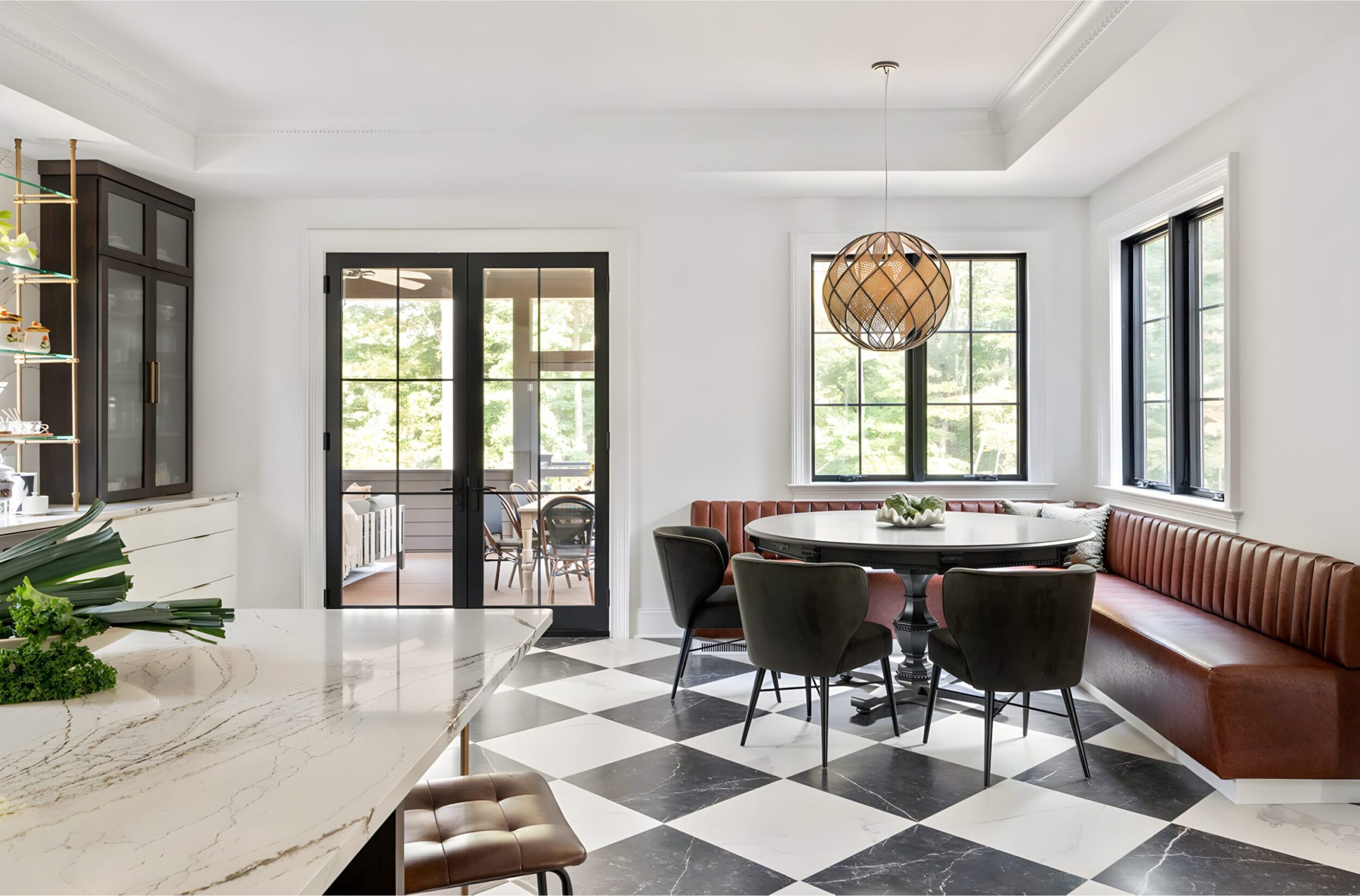 Kitchen dining nook with black round table, leather banquette seating, velvet chairs, and geometric pendant light