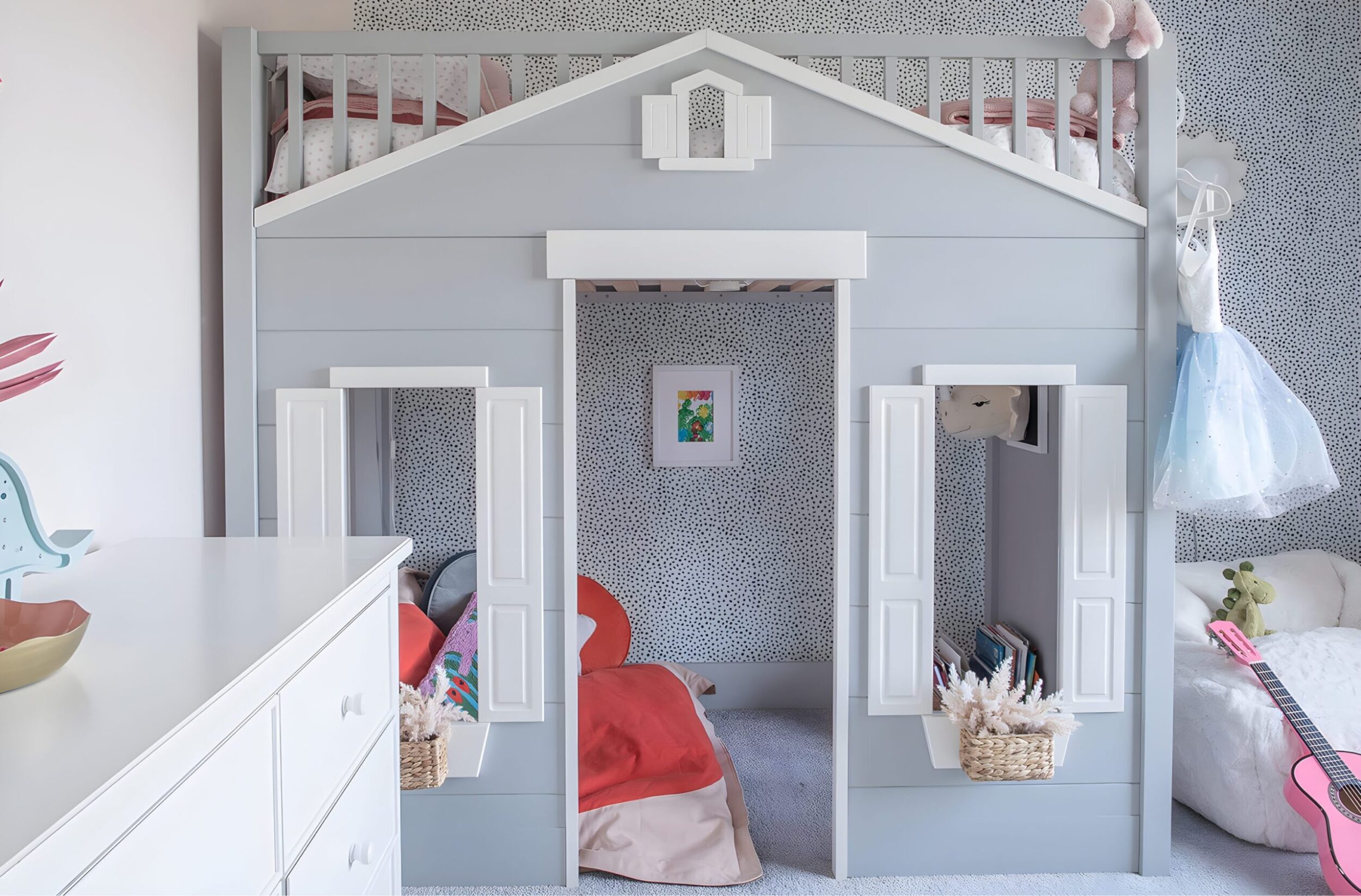 Girls’ room decor featuring pink curtains, dotted accent wall, loft play bed, and plush toys in bright space