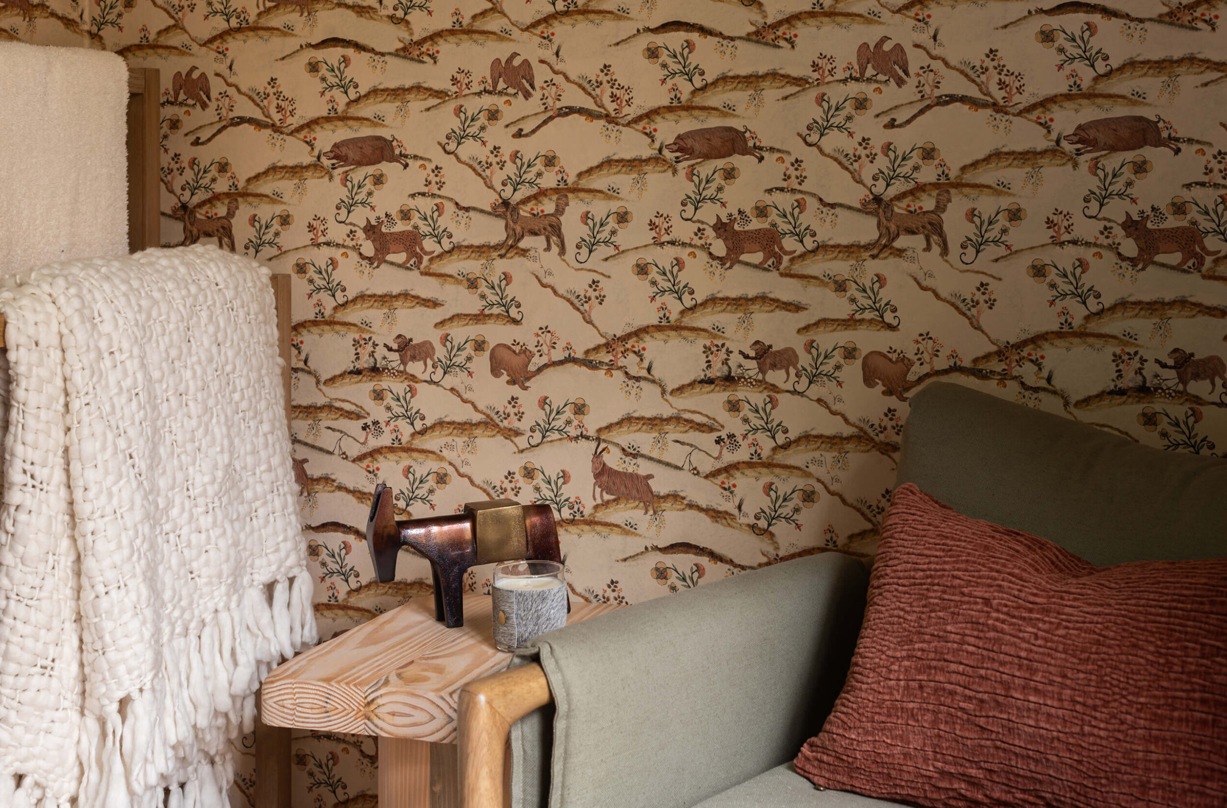 Cabin corner with earthy wallpaper, olive armchair, rust pillow, and wooden side table