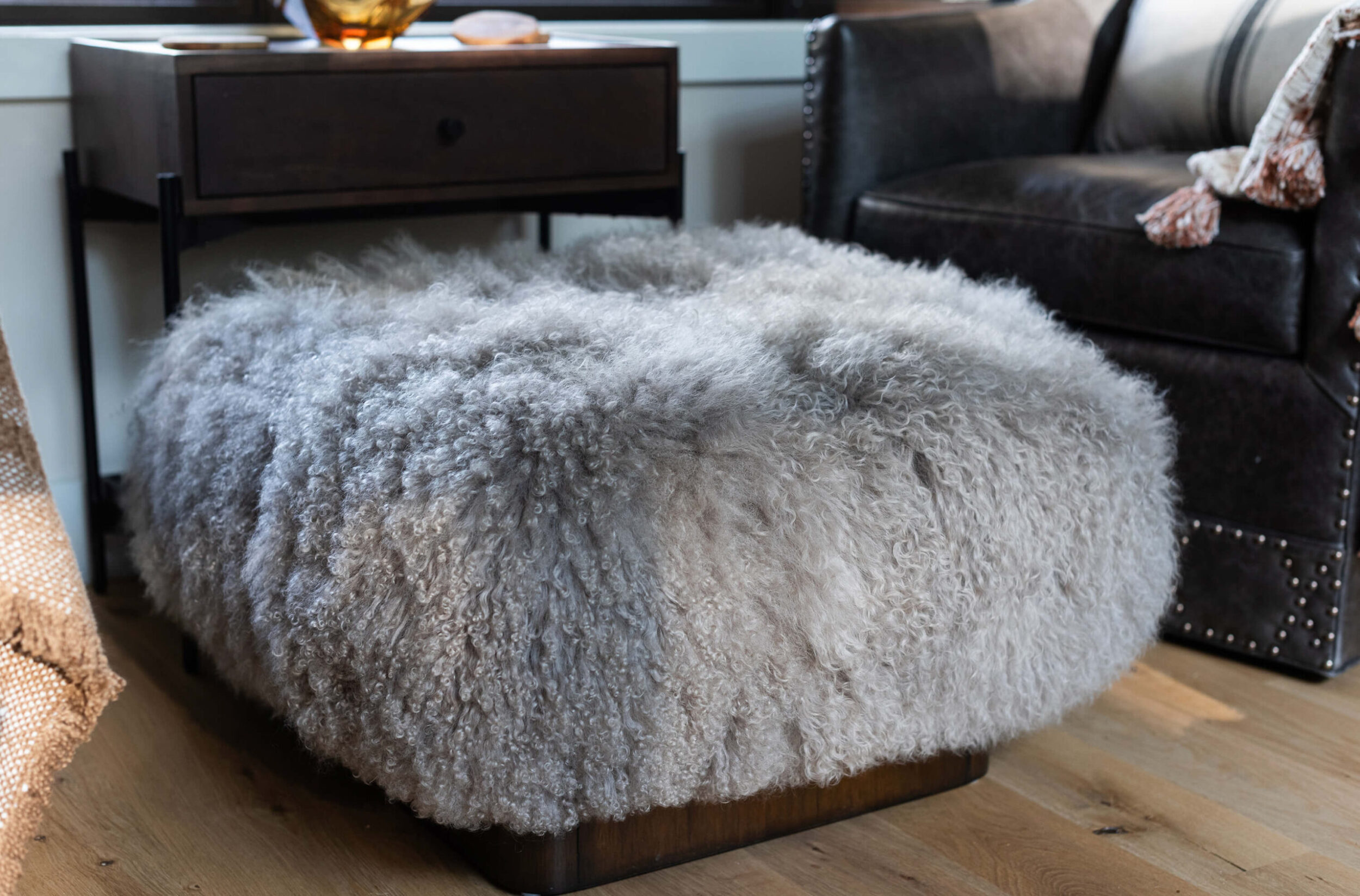 Fluffy gray sheepskin ottoman placed beside leather armchair and window in rustic modern cabin living space