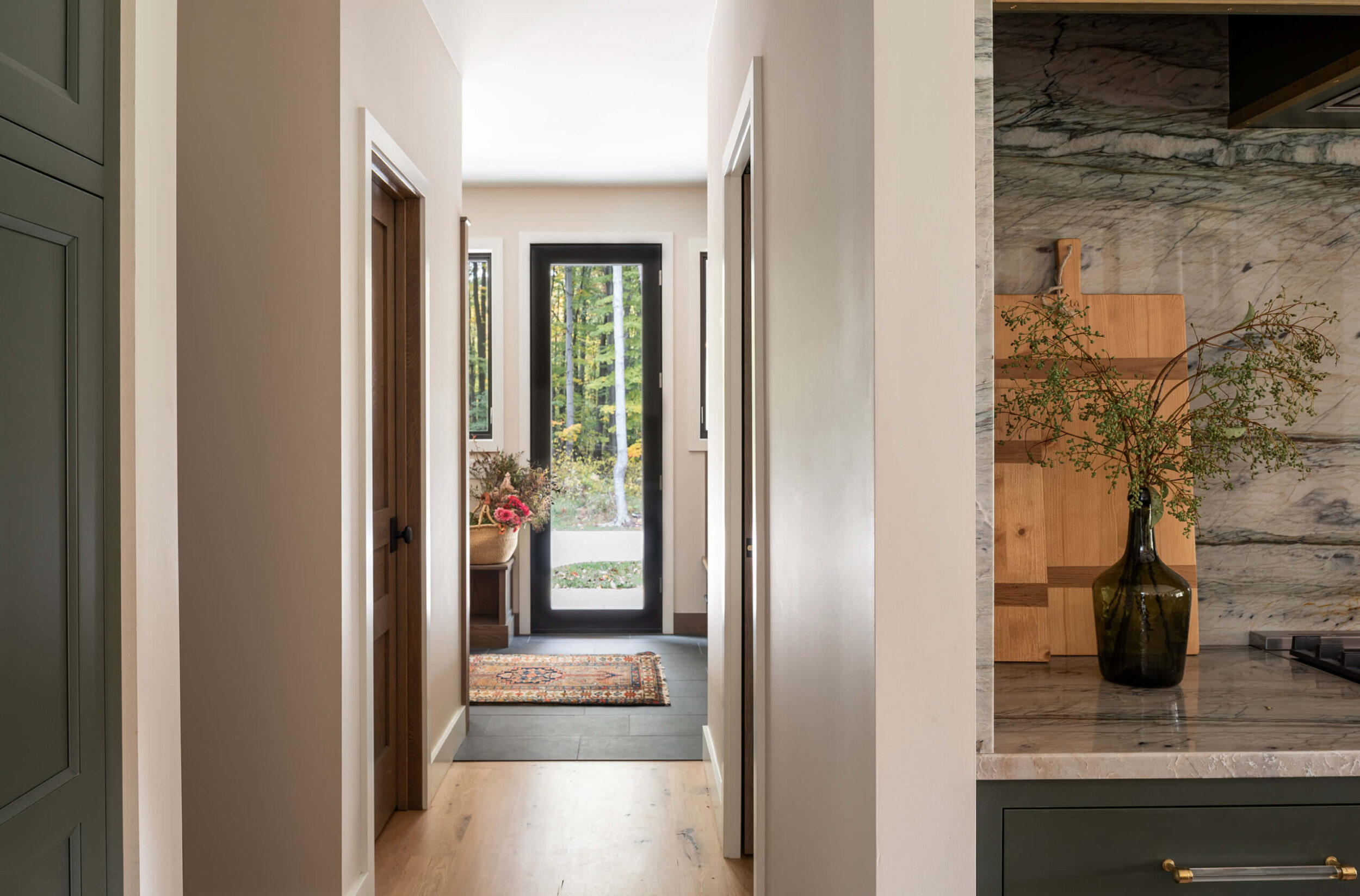 Hallway view toward glass door with outdoor autumn scene, wooden floors, console table, and vase with fresh flowers