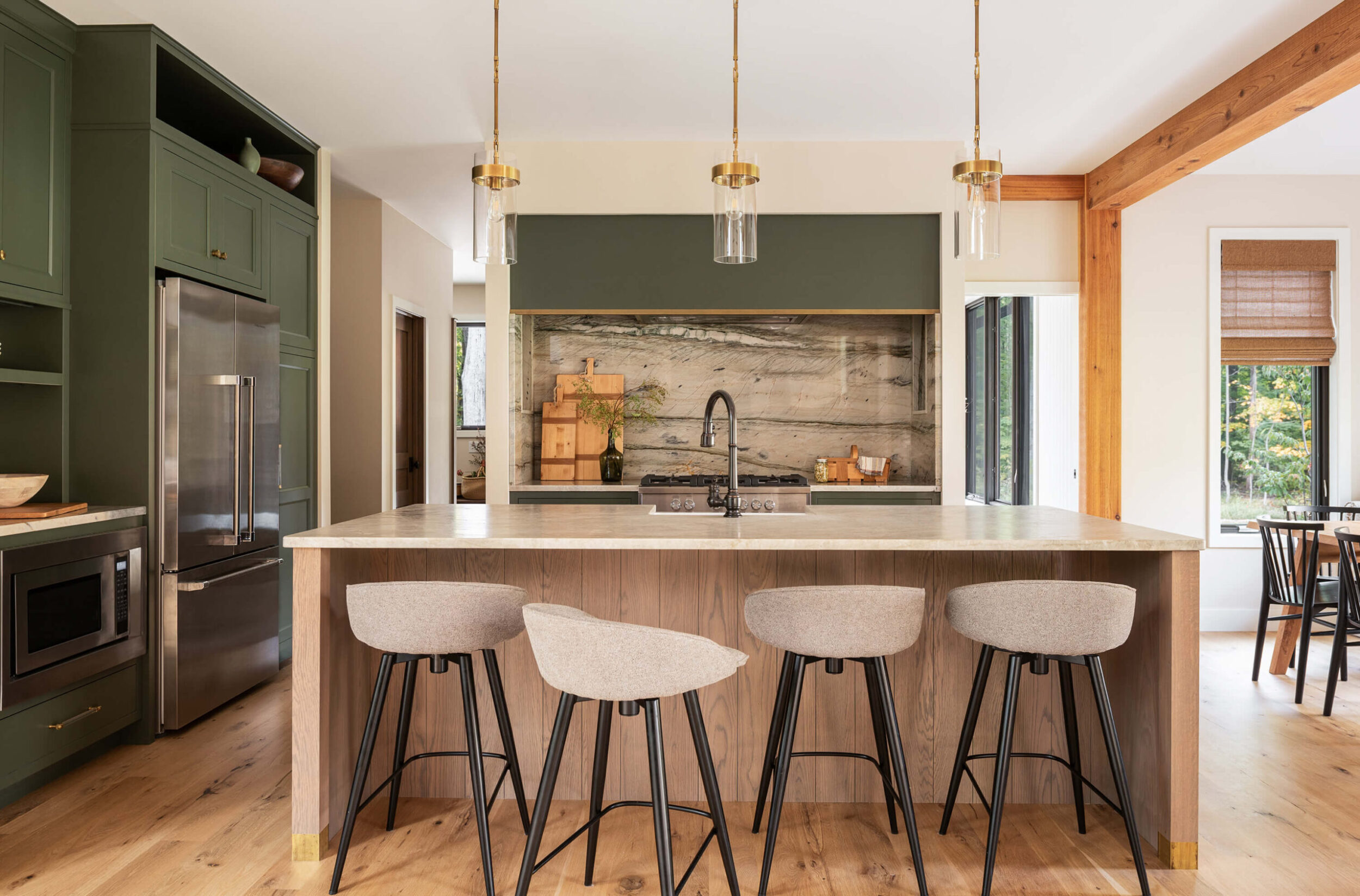 Modern kitchen with marble backsplash, island with stools, green cabinetry, brass pendant lights, and wood accents