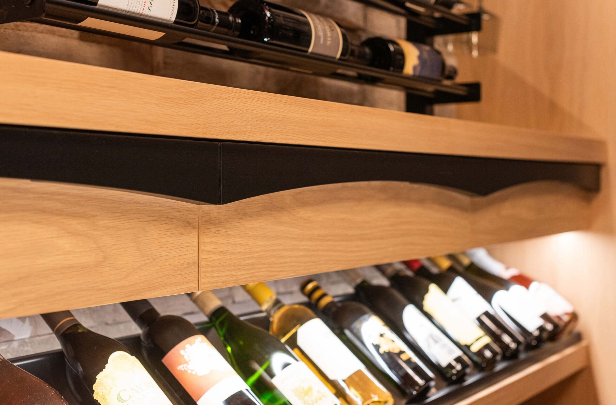 Close-up of wine cellar shelf with angled wooden frame, illuminated bottles of wine neatly arranged under modern racks